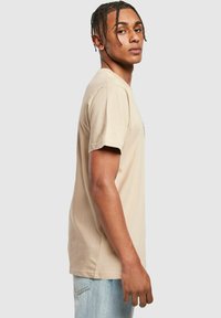 Beige bomull T-skjorte med korte ermer, rund hals og avslappet passform. Brukt med lyseblå denimjeans som viser en jevn tekstur.