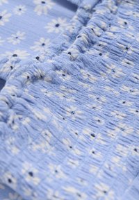 Ljusblått tyg med ett blommönster av små vita blommor och mörkblå mittar, med strukturerad samlad sömnad genom hela.