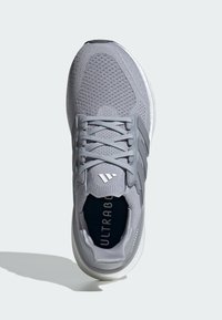 Sivi atletski tenisice s prozračnom mrežicom, s tri pruge kao naglasak, debelim bijelim potplatom i tiskanim oznakama "ULTRABOOST".
