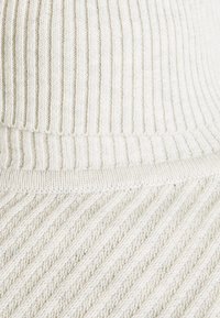 Pletená čepice v krémové barvě s vertikálními a diagonálními žebrovanými vzory, měkká na dotek a s přehnutým lemem.