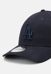 Casquette bleu marine avec logo "LA" brodé, visière incurvée et bande texturée hexagonale. Présente une forme ajustée et une étiquette taille moyenne-grande.