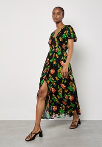 Blomster maxi kjole med sort baggrund, der har grønne blade og orange blomster. V-udskæring, korte ærmer og en høj slids for ekstra detalje.