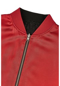Czerwona kurtka bomberka z satynowym wykończeniem, czarnym prążkowanym kołnierzem i złotym suwakiem. Wnętrze wykonane z teksturowanej, czarnej podszewki.