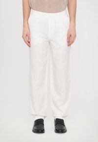 Pantalons en lin blancs avec une taille élastique, offrant une coupe décontractée et des poches latérales, associés à des chaussures noires.