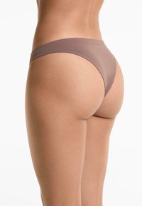 Bruine stringonderbroek met een gladde textuur, smalle tailleband en minimale bedekking. De stof lijkt zacht en rekbaar.