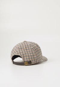 Beige, pruunide ja mustade toonidega houndstooth mustriga müts, millel on kõver visiit, ning pruun reguleeritav rihm taga.
