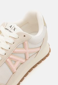 Baskets légères blanches avec des accents en suede beige, des détails de logo rose, un dessus en mesh texturé et une semelle en caoutchouc beige. Les lacets sont blancs.