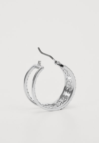 Brinco de argola prateada com um intrincado design recortado, apresentando uma borda texturizada e um fecho curvado para um fechamento seguro.