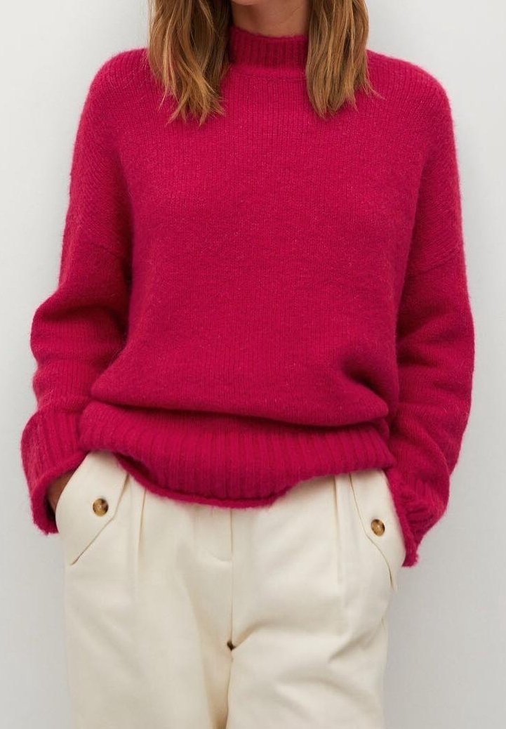 Pull en tricot fuchsia avec un col haut et des poignets côtelés, associé à un pantalon crème orné de deux boutons dorés.