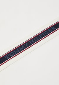 Sangle en tissu tissé avec une bande bleu marine et le texte brodé "TOMMY HILFIGER", bordée de rayures rouges et blanches.