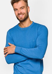 Niebieski bawełniany sweter z okrągłym dekoltem, z ribbowanymi mankietami i dołem. Posiada małe logo na piersi. Gładka tekstura i dopasowany krój.