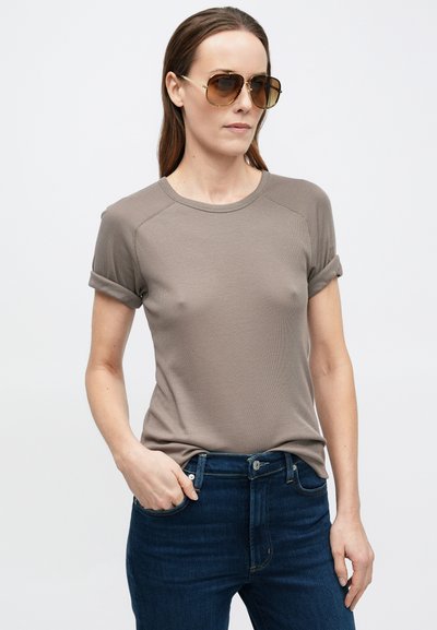 Bézs rövid ujjú póló felhajtott mandzsettákkal, bordázott textúrával, kerek nyakkivágással, sötétkék farmerral párosítva, semleges háttéren bemutatva.