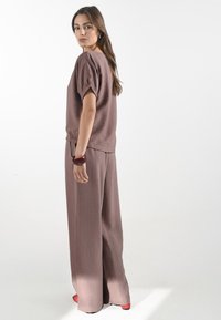 Losvallende, gestructureerde mauve top met korte mouwen en trekkoord aan de onderkant, gecombineerd met bijpassende wijde broek en een rode armband.
