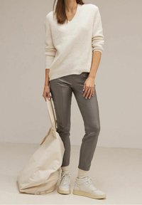 Krämfärgad stickad tröja med v-ringning, grå smal passform byxor, vita hög skor och en beige tygväska. Minimalistisk design och neutrala färger.