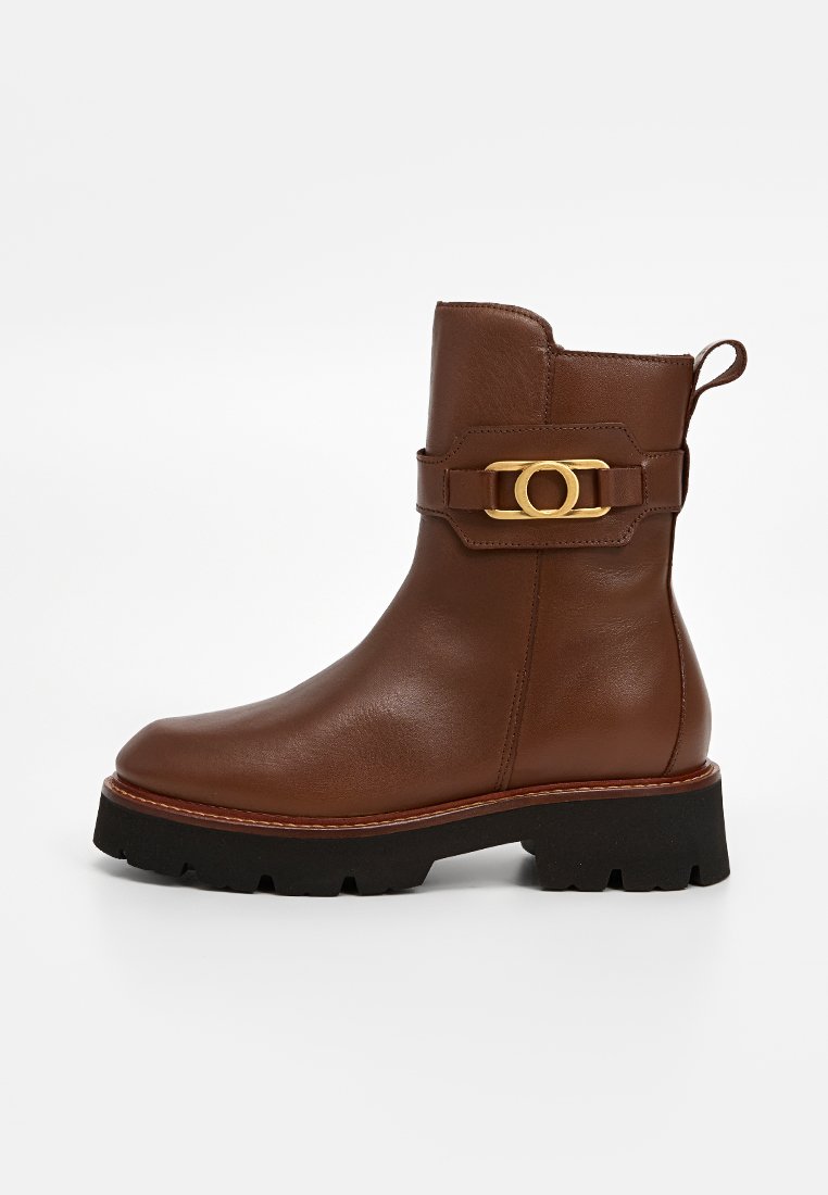 Braune Leder-Stiefelette mit einer kräftigen schwarzen Sohle, versehen mit einem dekorativen goldenen Schnallenriemen und einer Zuglasche an der Rückseite für einfaches Anziehen.