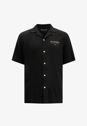 Chemise noire à manches courtes en tissu doux, avec un col pointu, une fermeture à boutons et un petit logo brodé sur la poitrine.