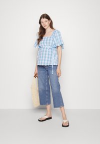 Top de mangas bufantes em padrão xadrez azul e branco, ajustado na cintura com uma fita, combinado com jeans azul de cintura curta e sandálias rasas. Bolsa tote de palha.