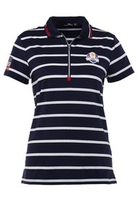 Polo bleu marine avec des rayures blanches horizontales, présentant une fermeture éclair courte et un petit patch drapeau américain sur la manche gauche. Accents rouges sur le col.