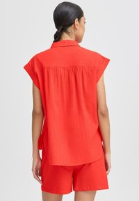 Blusa rossa a maniche corte con tessuto testurizzato e dettaglio sul retro, abbinata a pantaloni corti rossi coordinati, entrambi dal taglio morbido.