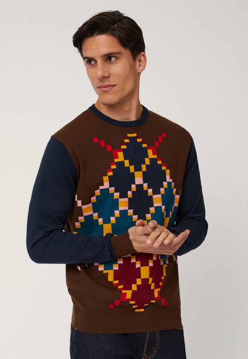 Bruin en marineblauwe trui met geometrisch meerkleurig patroon, met accenten in rood, geel, teal en roze. Ribgebreide manchetten en zoom.