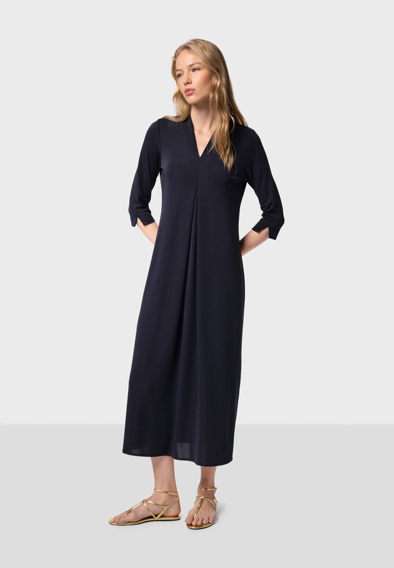 Vestido midi azul marino con escote en V y mangas tres cuartos, con detalle de plisado y tejido ligero. Combinado con sandalias doradas con tiras.