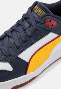 Navy leather sneaker with white, yellow, and burgundy accents. Features textured materials, round laces, and a padded tongue with logo.