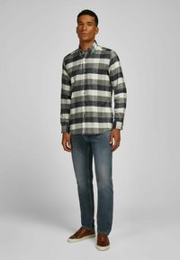 Flanellen overhemd in zwart-wit geruit patroon, met knoopsluiting, lange mouwen, gecombineerd met blauwe spijkerbroek en bruine sneakers.