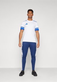 Sportswear set featuring a white short-sleeve T-shirt with blue accents and navy blue joggers with white side stripes. Lightweight fabric.