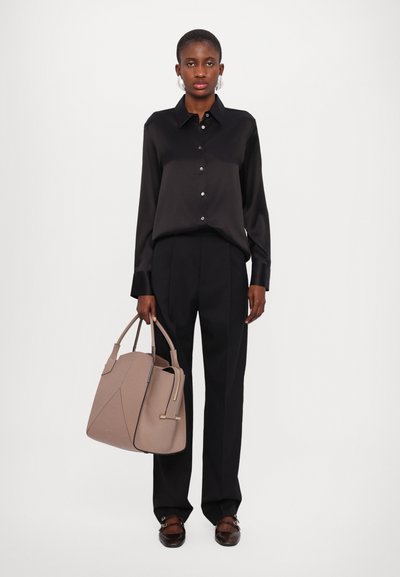 Chemise noire en satin à boutons, pantalon noir ajusté et sac à main structuré beige avec des accents géométriques. Des chaussures plates marron complètent le look.