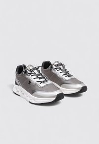 Baskets en maille grise avec des accents argentés, dotées d'un bout arrondi, d'un laçage, d'un col rembourré et d'une semelle blanche épaisse.