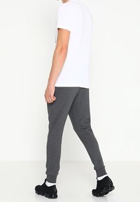 Grå sweatsbyxor med ribbad mudd, tillsammans med en enkel vit t-shirt. Outfitten inkluderar svarta sportskor och synliga vita strumpor.