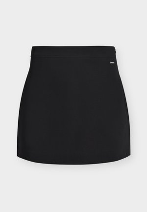 Mini-jupe droite noire avec une petite fermeture éclair latérale et une étiquette logo discrète sur la ceinture, sur fond blanc.