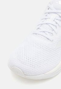 Zapatilla deportiva blanca con parte superior de malla transpirable, cordones planos y puntera redondeada, que presenta una suela de goma suave y un sutil detalle de marca.