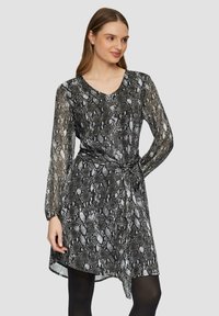 Zwart-wit slangenprint jurk met lange doorzichtige mouwen, V-hals, tailleband en asymmetrische zoomdetail. Gladde textuur.