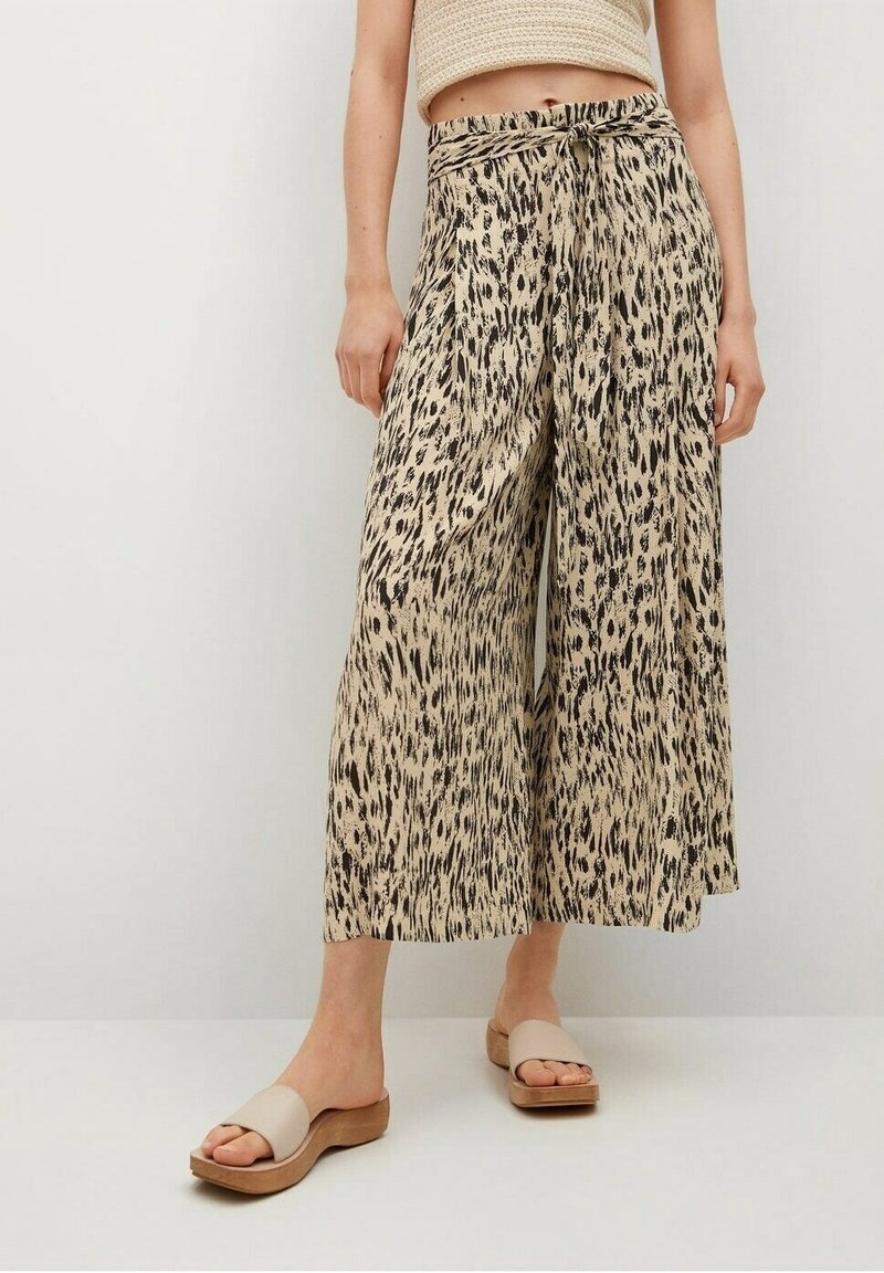 Culottes beige à jambes larges avec un motif animalier noir, dotées d'une ceinture à nouer et d'une texture lisse. Portées avec des sandales beiges plates.