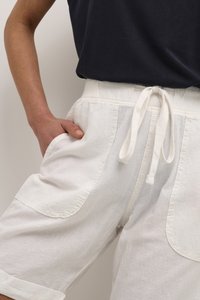 Pantalones cortos blancos hechos de un tejido texturizado, que cuentan con dos grandes bolsillos laterales y una cintura con cordón. Llevados con una parte superior oscura.