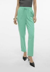 Mintgroene, lichtgewicht, elastische taillebroek met een strikdetail en recht model, gecombineerd met zwarte, puntige hakken.