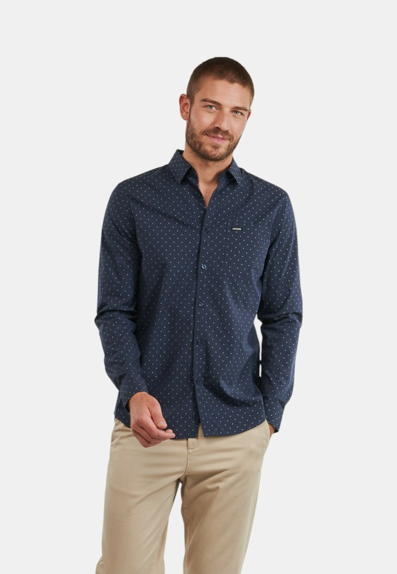 Camicia navy con bottoni, a pois bianchi piccoli, maniche lunghe e taschino sul petto. Realizzata in tessuto dalla superficie liscia.