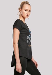 Svart t-skjorte med korte ermer, med grafisk trykk på framsiden. Stoffet ser mykt ut med en avslappet passform og en litt buet kant.