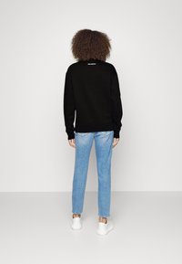 Felpa nera con maniche lunghe, polsini e orlo a coste, abbinata a jeans azzurri e sneakers bianche, vista dal retro.