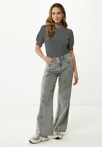 Camicia fitted a righe bianche e nere con maniche corte a sbuffo, abbinata a jeans grigi a gamba larga a vita alta. Sneakers grigie completano il look.