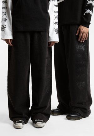 Black wide-leg pants made of soft material, featuring faded graphic prints and subtle texture details on the fabric. Worn with contrasting footwear.