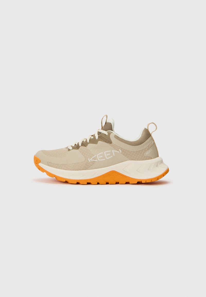 Zapatilla deportiva beige con suela naranja, de material sintético y malla, media suela acolchada, cordones y detalle de logo en el lateral. Diseño ligero.