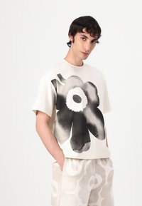 Krämfärgad t-shirt med ett stort svart blommönster, korta ärmar, avslappnad passform. Tyg liknande bomull, i kombination med ljusa mönstrade shorts.