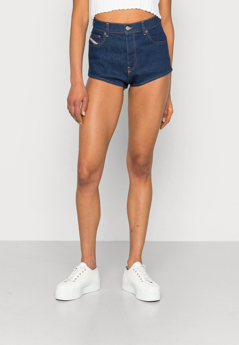 Shorts de mezclilla oscuros de tiro alto con un diseño ajustado, que cuentan con bolsillos frontales y detalles de costura, combinados con zapatillas de plataforma blancas.