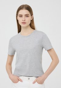 Maglietta grigia a maniche corte in materiale morbido con scollatura rotonda. Il tessuto ha una leggera texture ed è abbinato a pantaloni bianchi.
