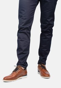Zapatos de cuero marrón con un acabado suave, puntera redonda y suela de goma blanca. Chinos navy con un corte recto y un leve brillo.