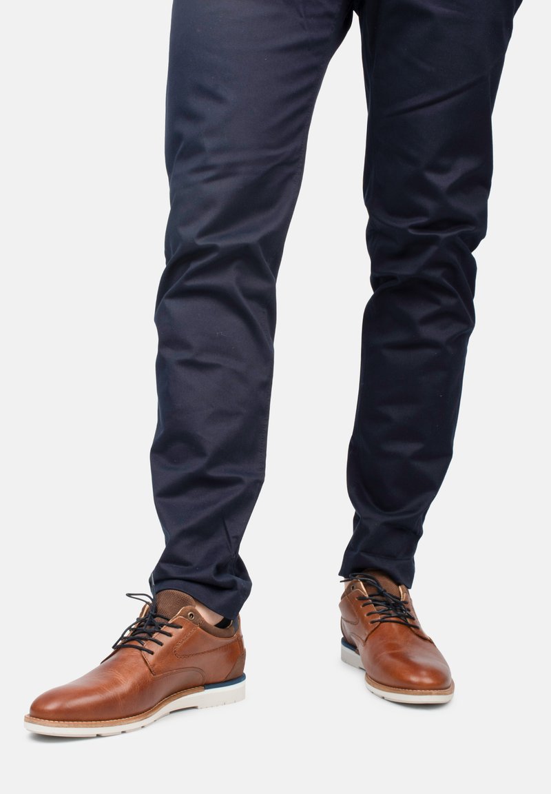 Zapatos de cuero marrón con un acabado suave, puntera redonda y suela de goma blanca. Chinos navy con un corte recto y un leve brillo.