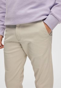 Pantalon en coton beige avec une texture lisse et des poches latérales, associé à un sweat-shirt violet clair avec un design en polaire douce.