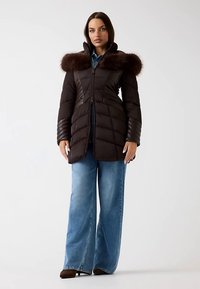 Doudoune noire avec un col bordé de fourrure, dotée d'une fermeture éclair à l'avant et d'un design matelassé vertical ; portée avec un jean denim à jambes larges.